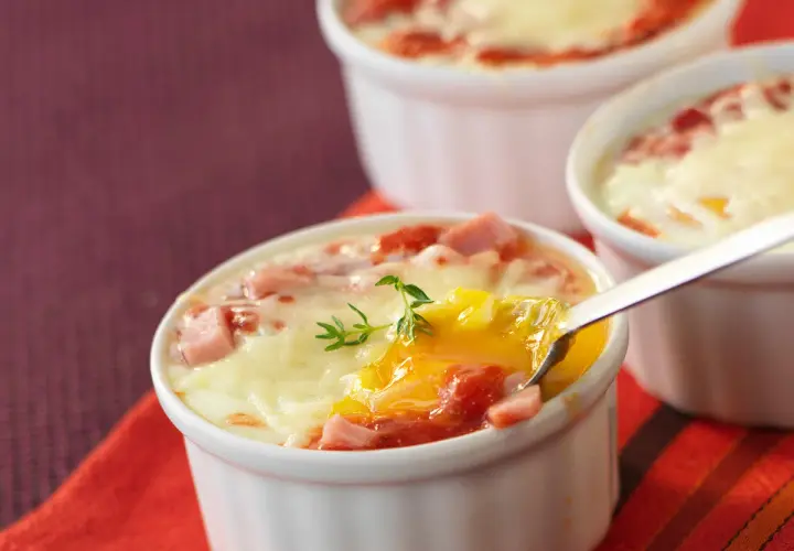 Œufs cocotte au four, jambon et fromage fondus, un délice crémeux prêt à être dégusté.