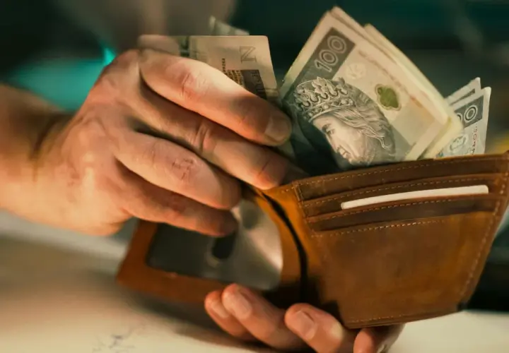 Dłonie wkładają polskie banknoty do brązowego portfela. Czy to już netto, czy jeszcze brutto?
