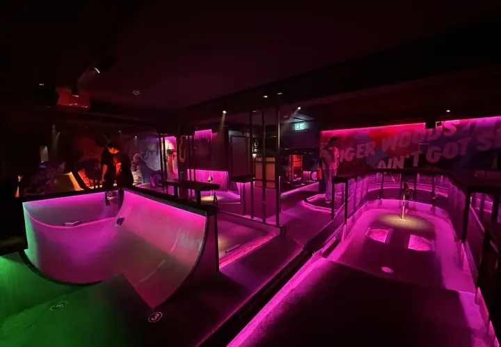En neonupplyst minigolfbana i Göteborg med rosa och grönt ljus. En person står vid en bana.