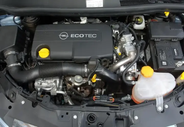 Silnik Opel Corsa D 1.2 benzyna. Widoczny jest czarny dekiel z napisem Ecotec, akumulator Varta oraz zbiornik płynu chłodniczego.