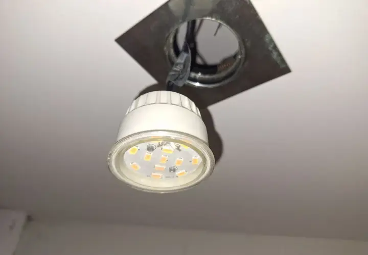 Wymiana żarówki LED GU10: widoczna jest nowa żarówka LED GU10 wisząca obok oprawy sufitowej, gotowa do montażu.