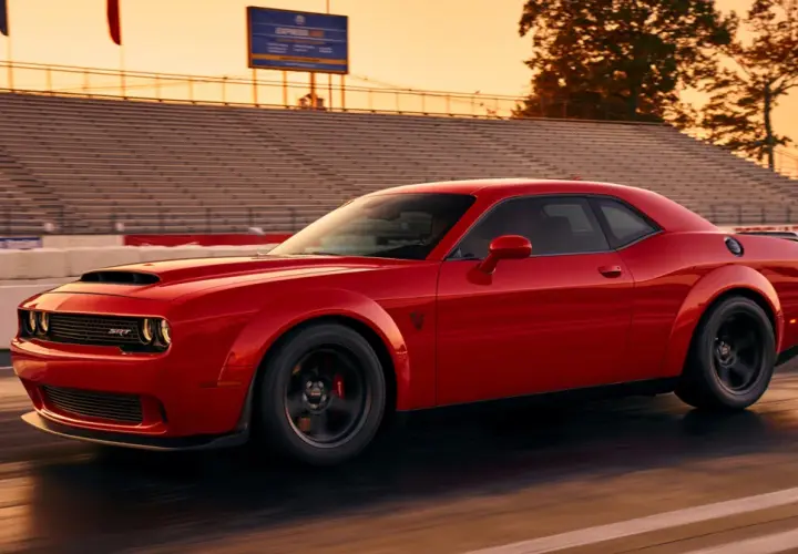 Czerwony Dodge Challenger SRT pędzi po torze wyścigowym podczas zachodu słońca, z trybunami w tle.