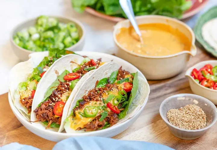 Tacos med koreansk pulled pork, toppade med sallad, chili och sesamfrön. Serveras med en krämig sås och färska grönsaker.