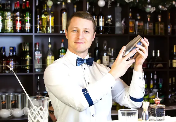 Uśmiechnięty barman z shakerem w dłoniach, za nim półki z alkoholem. Zastanawiasz się, ile zarabia barman za granicą?