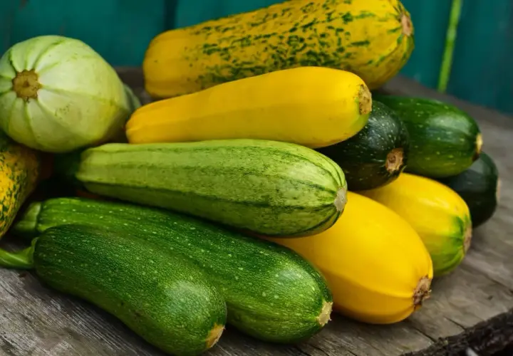 Un tas de courgettes vertes et jaunes, dont une courgette blanche pâle, reposent sur des planches de bois.