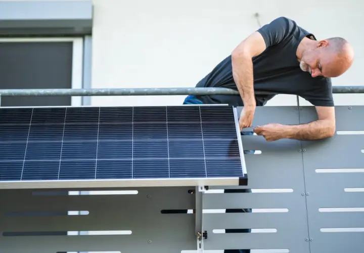 Mann montiert Solarmodul auf einem Balkongeländer.