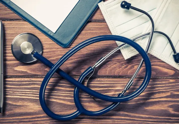 Stetoscopio, penna, cartella e mascherina su tavolo di legno. Preparativi per aprire studio medico in appartamento.