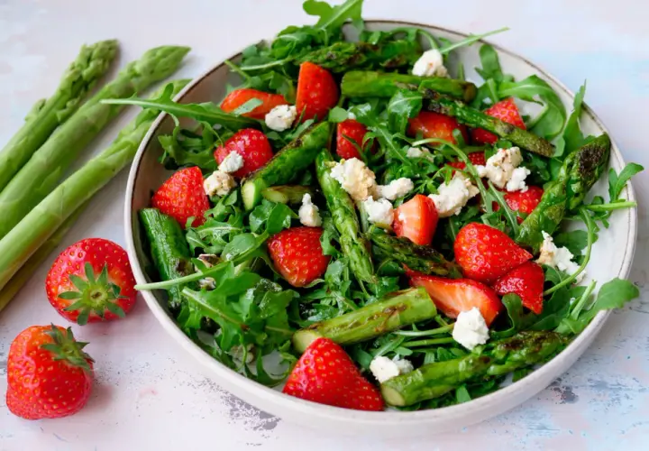 Frischer Spargelsalat mit Erdbeeren und Rucola, garniert mit zerbröseltem Käse.