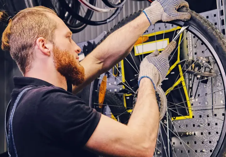 Mechanik w rękawiczkach naprawia **detkę** w rowerze, używając łyżki do opon.