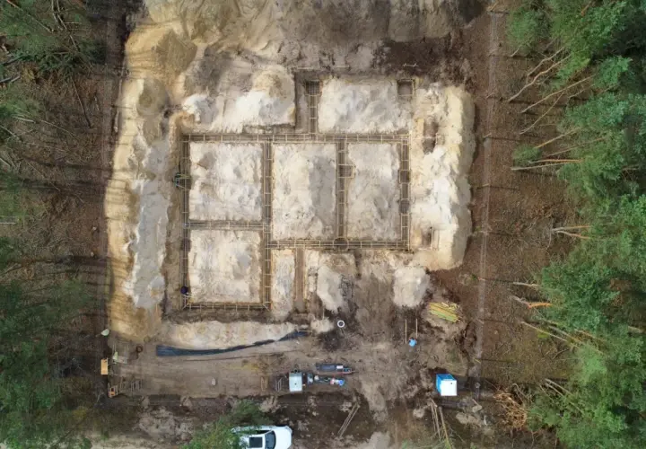 Budowa fundamentów domu w lesie. Widać zbrojenie i szalunki. W tle drzewa. To etap prac poprzedzający badania geotechniczne gruntu.