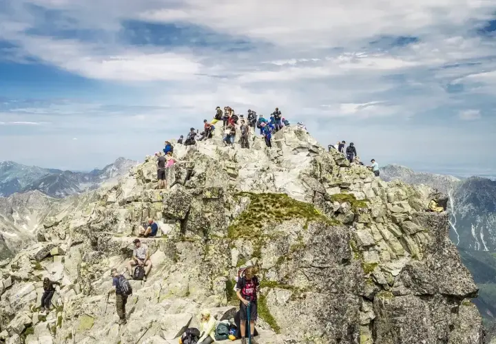 Tłum turystów na skalistym szczycie, najwyższy szczyt w Polsce, Rysy, podziwia panoramę Tatr.
