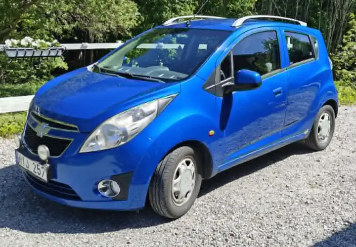Blå Chevrolet Spark med extraljus, kanske ett problem med bilen? Parkerad på grusväg.