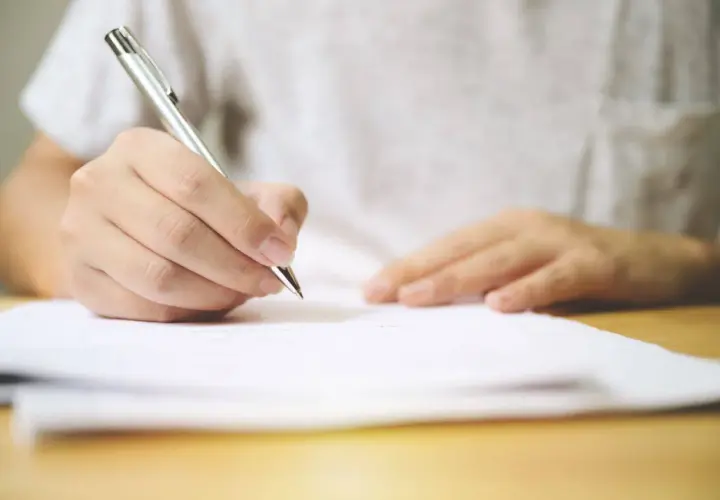 Dłoń pisze długopisem na dokumencie. Umowa najmu na czas określony przechodzi na czas nieokreślony.