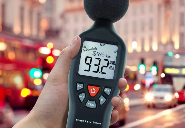 Mano sosteniendo un medidor de sonido para medir db en una calle ruidosa de la ciudad.
