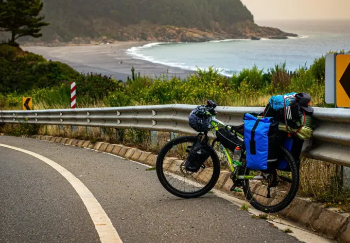 Rower MTB gotowy do bikepackingu, zapakowany przy drodze z widokiem na ocean i plażę.