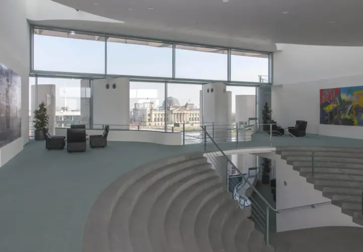 Modernes Foyer im Bundeskanzleramt mit Blick auf das Reichstagsgebäude. Sitzgruppen und eine geschwungene Treppe laden zum Verweilen ein.