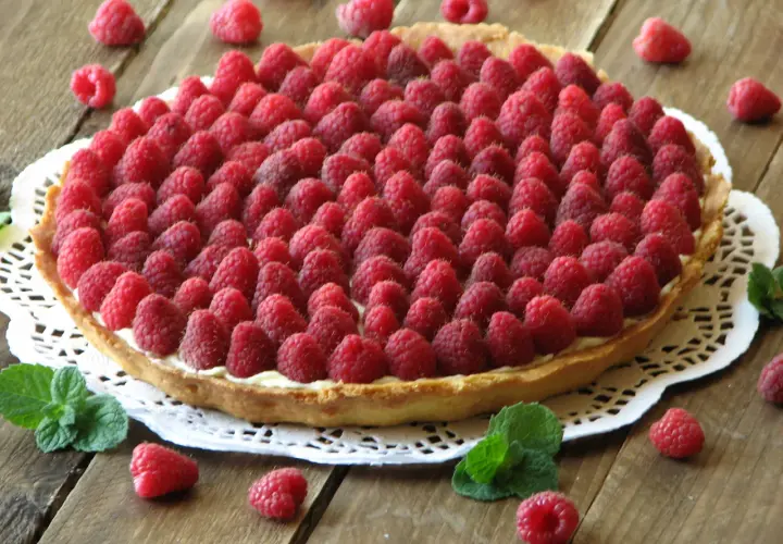 Pyszna tarta z malinami, udekorowana świeżymi listkami mięty. Idealna na letnie popołudnie.