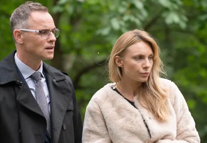 Adam i Ewa obsada: mężczyzna w okularach i płaszczu oraz kobieta w futrzanej kurtce na tle zieleni.