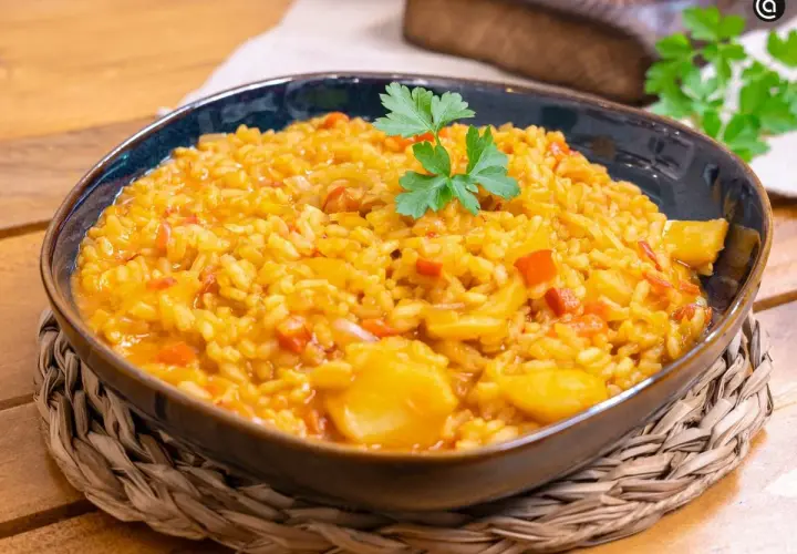 Un plato humeante de arroz con bacalao, adornado con perejil fresco, servido en un cuenco azul sobre una esterilla de mimbre.