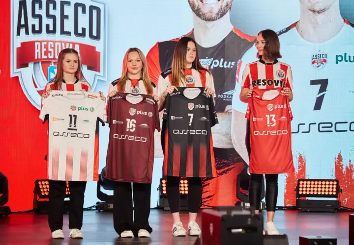Cztery młode kobiety prezentują koszulki siatkarskie drużyny Asseco Resovia. Dwie w białych, dwie w ciemnych strojach.