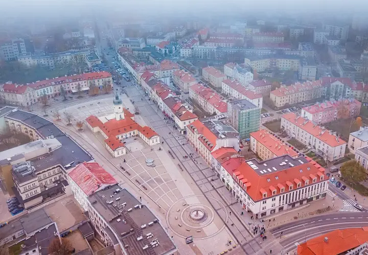 Widok z lotu ptaka na rynek Kościuszki w Białymstoku, otoczony kamienicami i budynkiem ratusza.
