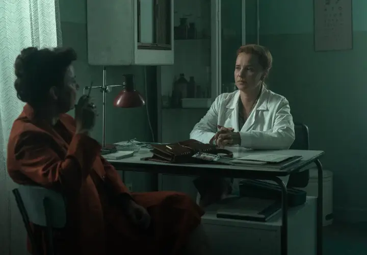 Dwie kobiety w gabinecie lekarskim. Jedna w białym kitlu, druga w pomarańczowym płaszczu, pali papierosa. Czy to scena z filmu "Ołowiane dzieci" czy na faktach?