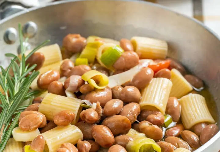 Minestra di fagioli con pasta rigata, cipollotto e rosmarino in una padella.