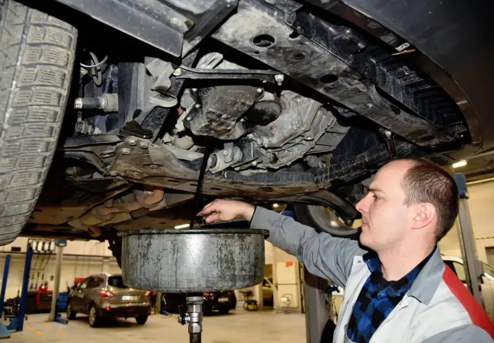 Mechanik spuszcza olej z samochodu. Pamiętaj o regularnej wymianie oleju w samochodzie co ile kilometrów, by silnik działał sprawnie.