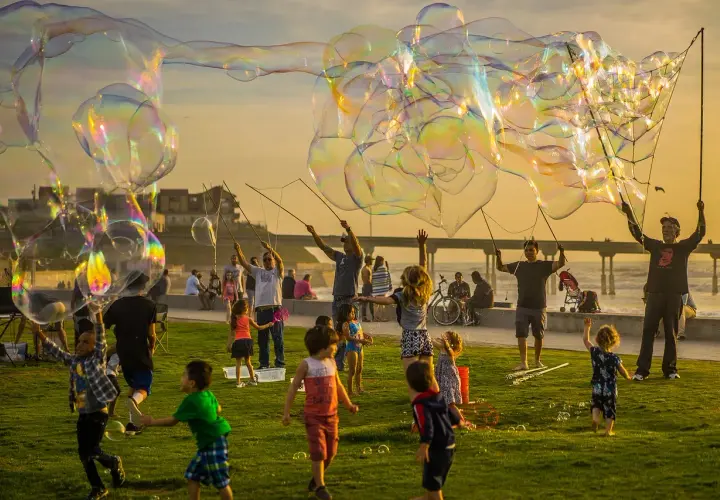 Un compleanno alternativo per bambini con bolle giganti al tramonto. Bambini e adulti si divertono a creare enormi bolle iridescenti sulla costa.