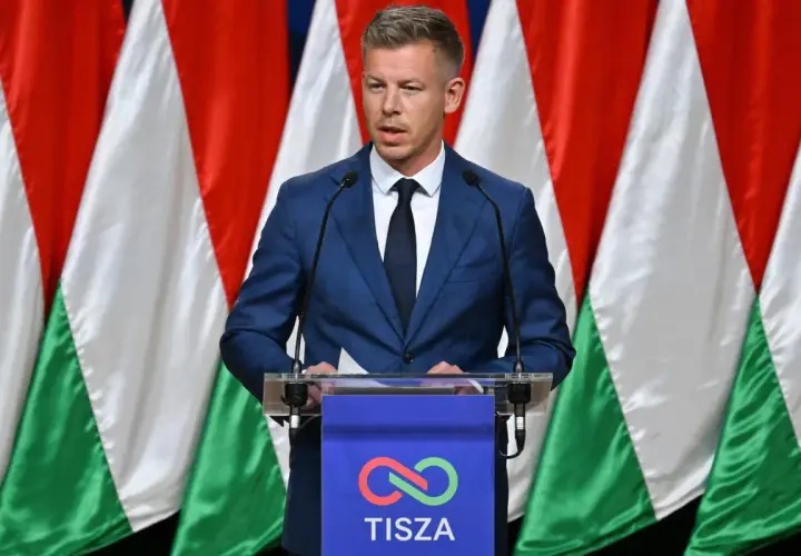 Mężczyzna w garniturze przemawia na tle flag Węgier. Dyskusja o węgry liczba ludności.