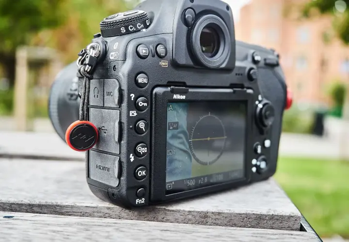 Nikon D850 test w plenerze. Aparat leży na drewnianym stole, w tle zieleń i budynek.