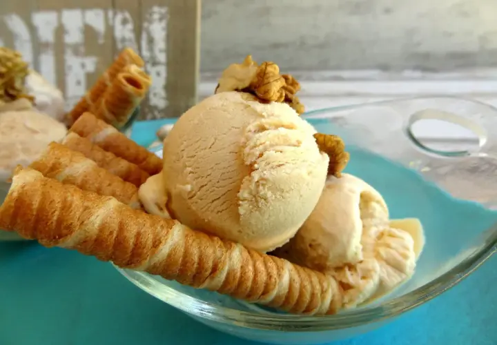 Delicioso helado de dulce de leche con barquillos crujientes y nueces, servido en un cuenco de vidrio sobre un plato turquesa.
