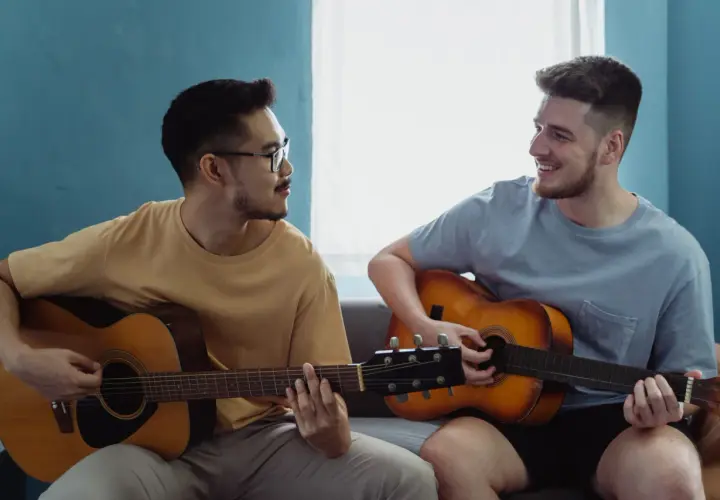Dwóch mężczyzn gra na gitarach akustycznych. Jeden z nich ma okulary, drugi uśmiecha się.