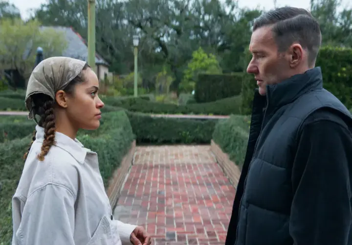 Due persone si guardano in un giardino curato, con siepi e un vialetto di mattoni. Le recensioni per "il maestro giardiniere" potrebbero descrivere scene come questa.