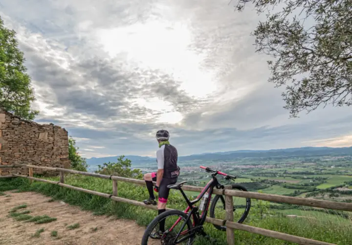 Ciclista descansa junto a su bici en ruinas de coll sa cabra, contemplando el valle.