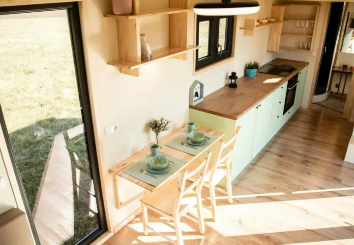 Gemütliches tiny house innen mit Esstisch, Küche und Blick ins Grüne.