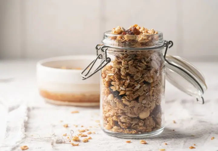 Barattolo di vetro pieno di granola fatta in casa, con fiocchi d'avena, frutta secca e noci.