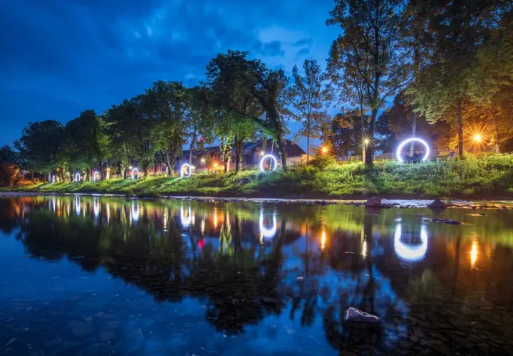 Nocny spacer wzdłuż rzeki, gdzie świetliste kręgi odbijają się w wodzie. Magiczna atmosfera, która płynie przez Cieszyn.