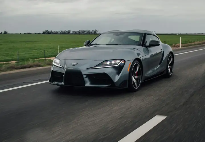 Szare auto sportowe jedzie po drodze. Ciemne felgi świetnie komponują się z nadwoziem, odpowiadając na pytanie: jaki kolor felg do srebrnego auta?