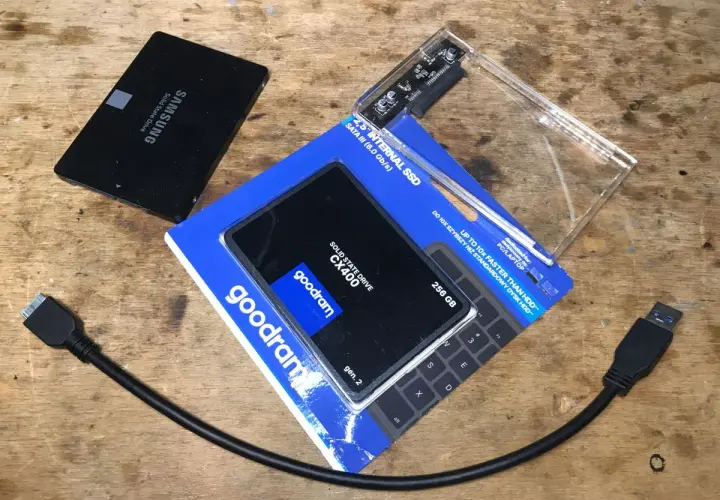 Dwa dyski SSD, jeden Samsung, drugi Goodram CX400 256 GB, obok obudowa na dysk i kable SATA.