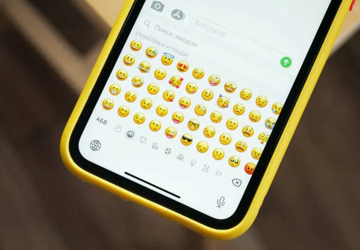 Na ekranie telefonu w żółtej obudowie widać klawiaturę z mnóstwem wesołych i smutnych emotek.