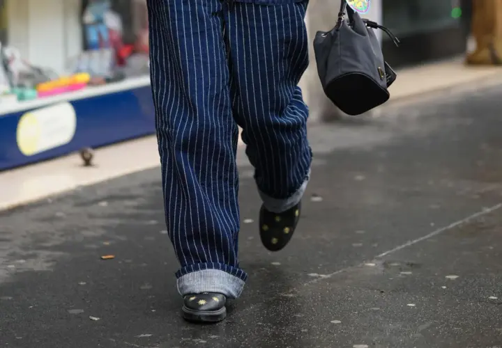 Person mit gestreiften Hosen, die die Jeans umschlagen. Schwarze Schuhe mit Sternenapplikationen und eine kleine Tasche.