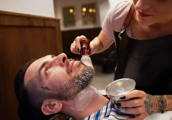 Barberka nakłada pianę do golenia na brodę klienta pędzlem.