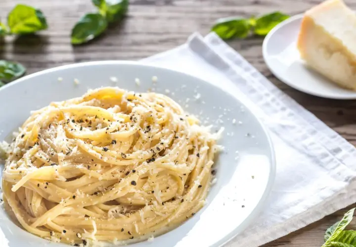 Szybki obiad z makaronem: spaghetti posypane parmezanem i pieprzem, obok kawałek sera i listki bazylii.