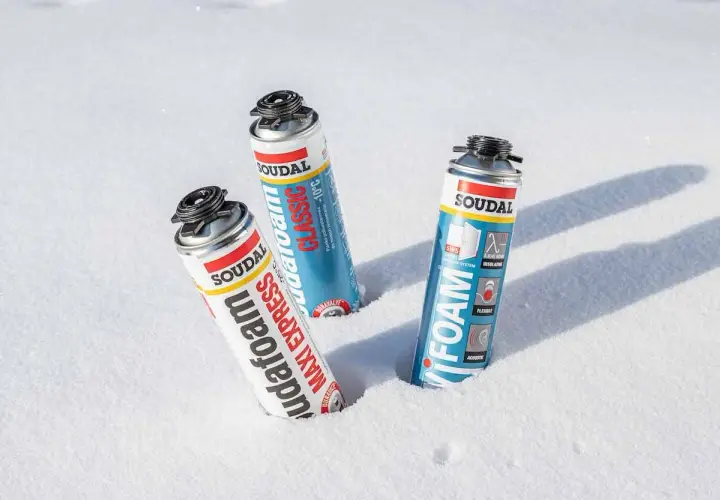 Trzy puszki pianki montażowej zimowej Soudal w śniegu. Pianka "Maxi Express" i "Classic" obok siebie, a dalej "Foam".