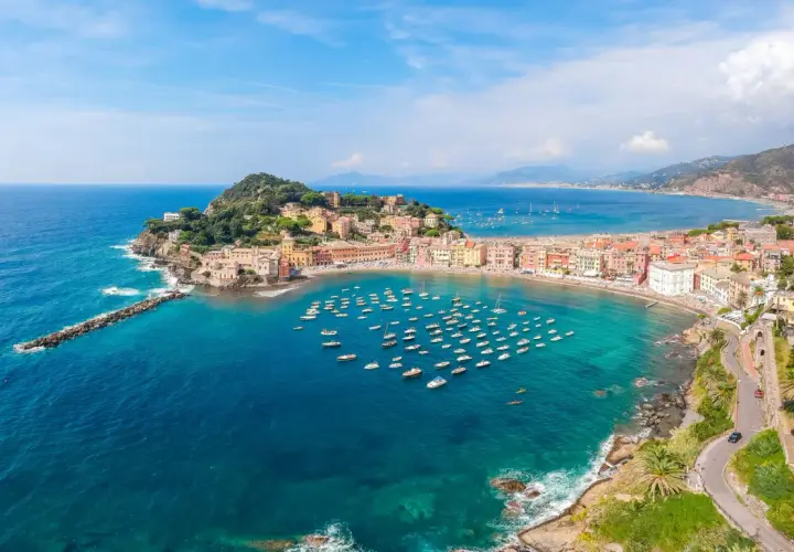 Vue aérienne de la baie de Sestri Levante, avec ses maisons colorées, sa plage et une multitude de bateaux dans les eaux turquoise.