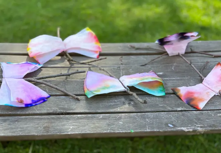 Bunte Schmetterlinge aus Kaffeefiltern, die Kinder leicht selber machen können, sitzen auf einem Holzbrett.