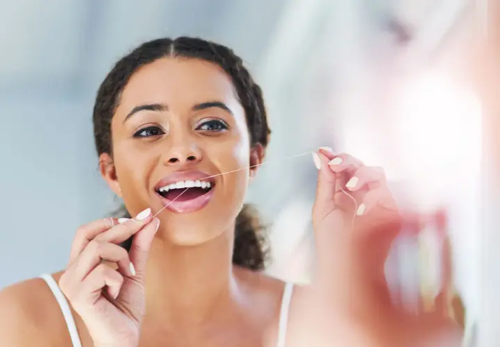 Donna sorridente usa il filo interdentale, un gesto quotidiano per un sorriso sano. Quante volte usare il filo interdentale? Almeno una volta al giorno.