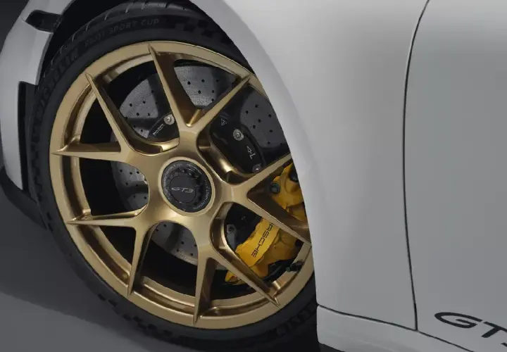 Detalle de un coche deportivo blanco con llantas doradas y pinzas amarillas. Se aprecian los discos de **frenos cerámicos** perforados, listos para la acción.