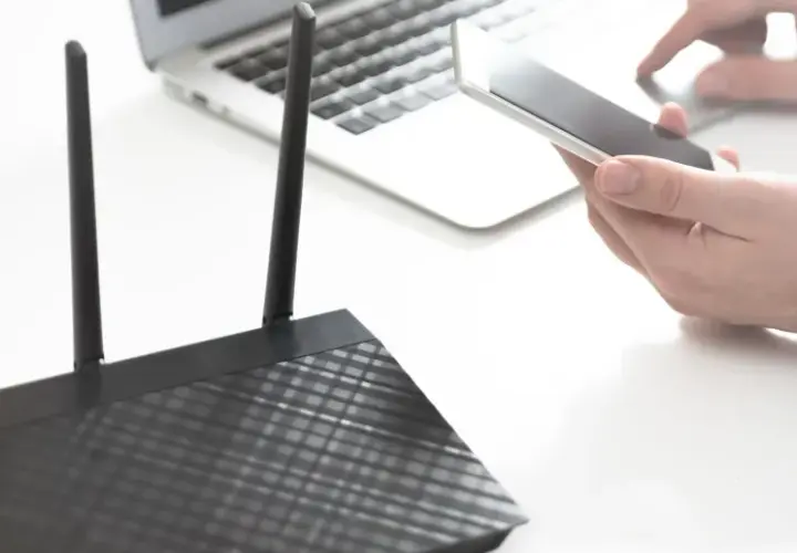 Osoba trzyma smartfon obok laptopa i routera, pokazując, jak udostępnić internet z telefonu na komputer przez USB.